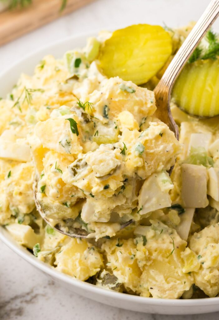 A serving scoop of the potato salad with dill pickles and fresh dill