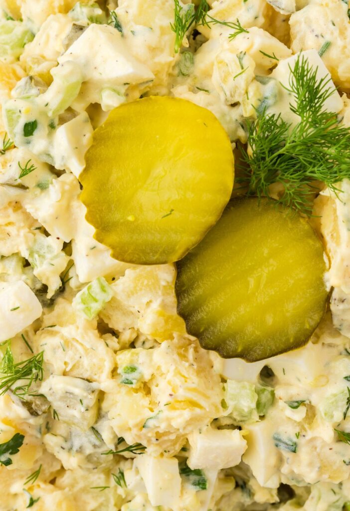 Close up of the potato salad with fresh dill and dill pickle slices on top.