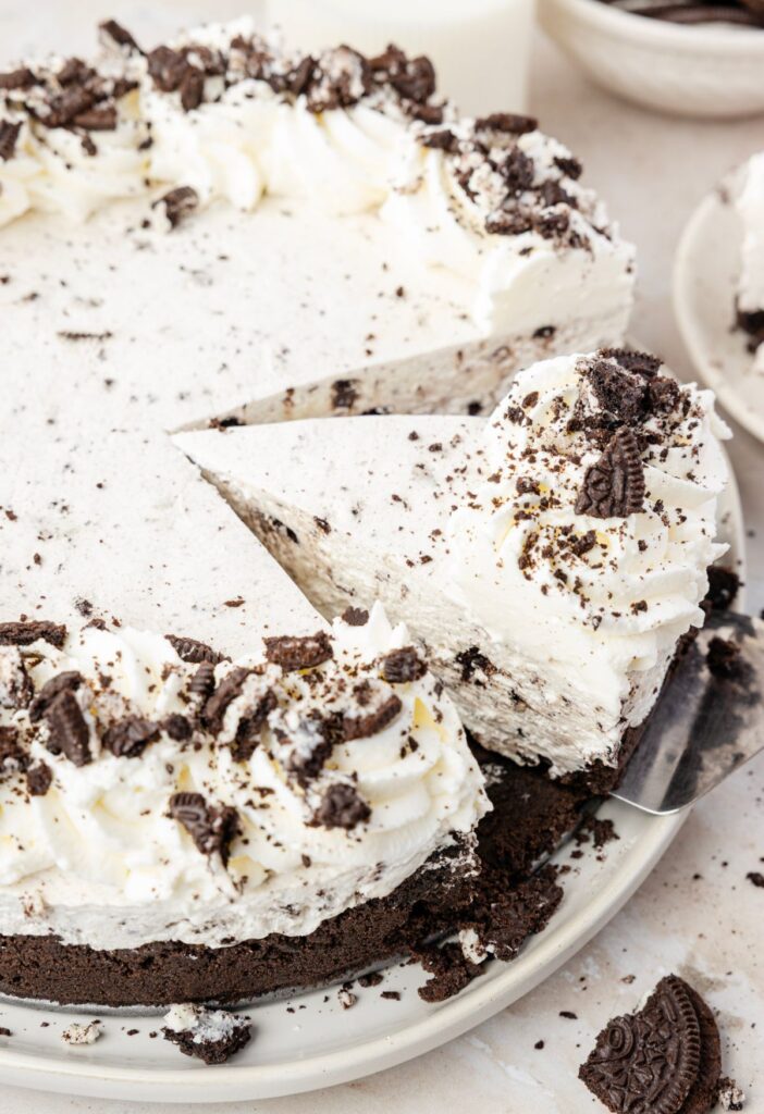 A oreo cheesecake cut into slices with a serving spatula taking a slice out of the cheesecake.