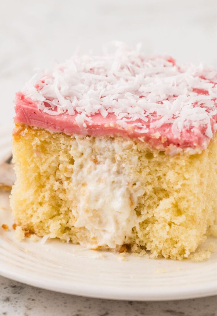 A slice of cake with cream filling and raspberry coconut topping.