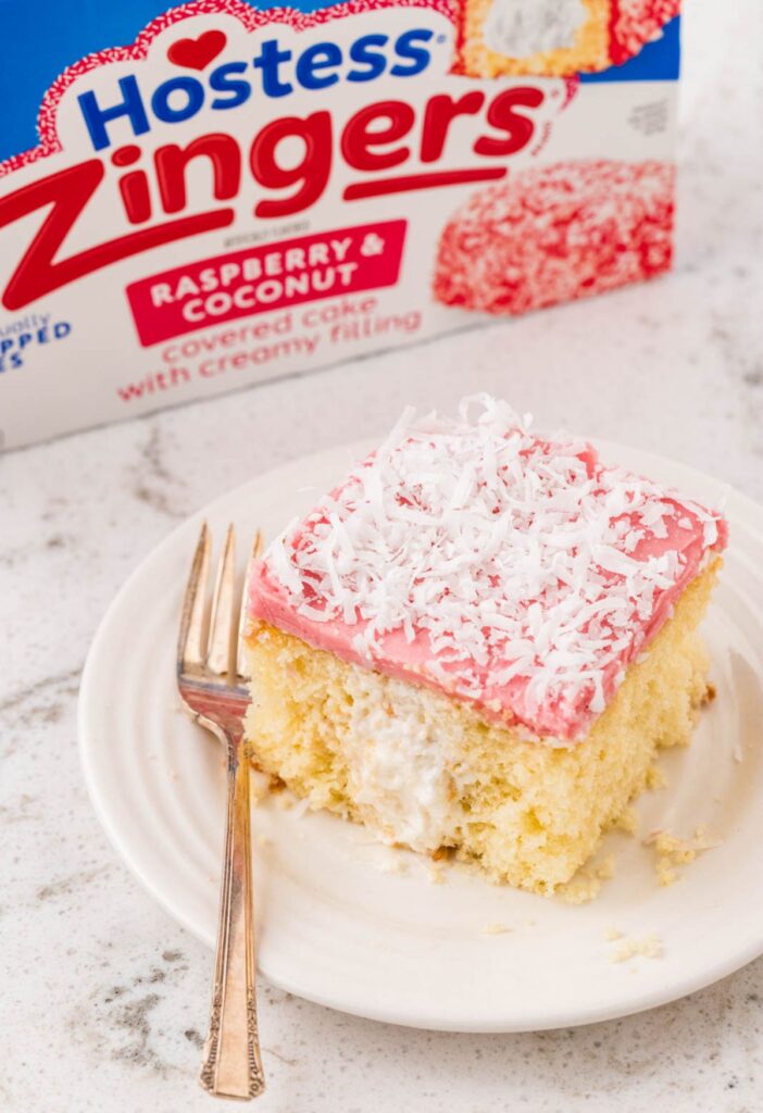 A piece of the hostess raspberry zingers cake on a plate with a box if the snack cakes behind it.