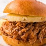 A pulled pork sandwich with a pineapple ring on it.
