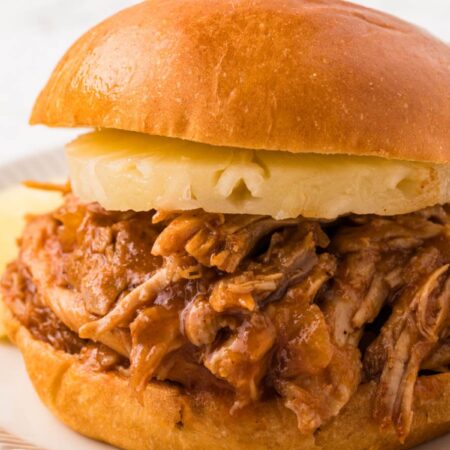 A pulled pork sandwich with a pineapple ring on it.