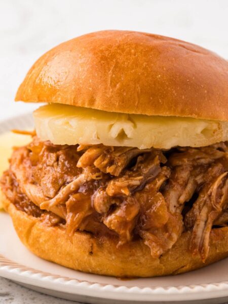A pulled pork sandwich with a pineapple ring on it.