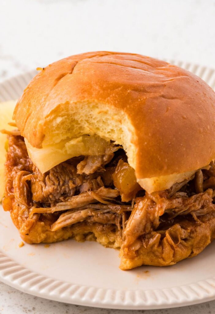 A shredded pulled pork sandwich with a bite taken out of it.