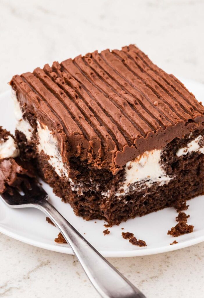 A slice of cake with a fork bite taken out of the corner of it.