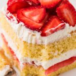 A slice of layered strawberry shortcake with a fork bite taken out of the front.