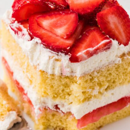 A slice of layered strawberry shortcake with a fork bite taken out of the front.