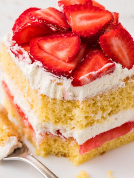 A slice of layered strawberry shortcake with a fork bite taken out of the front.