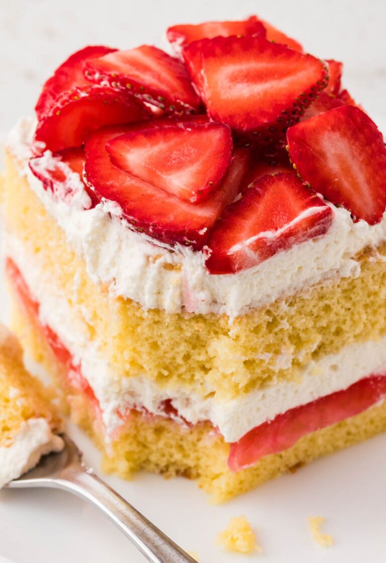 A slice of layered strawberry shortcake with a fork bite taken out of the front.