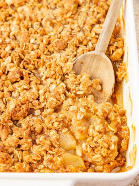 A pan of applesauce crisp with a wooden serving spoon inside of it.