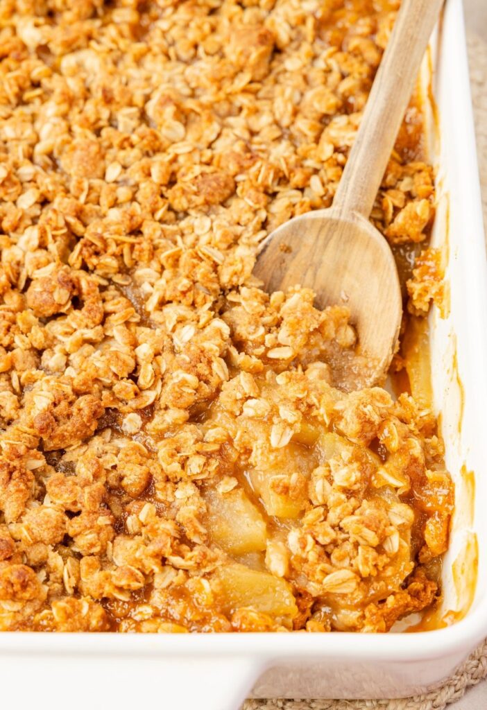 A pan of applesauce crisp with a wooden serving spoon inside of it.