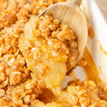 A wooden spoon holding some of the applesauce crisp on it above the pan of apple crisp below it.