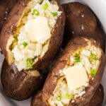 Baked potatoes inside the slow cooker cut open with butter in them.