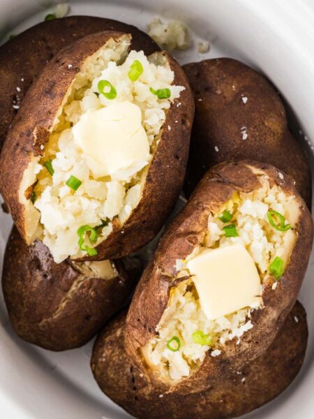 Baked potatoes inside the slow cooker cut open with butter in them.