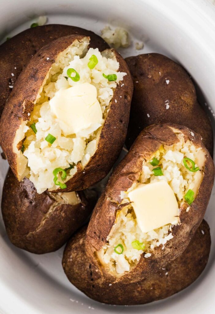 Baked potatoes inside the slow cooker cut open with butter in them.