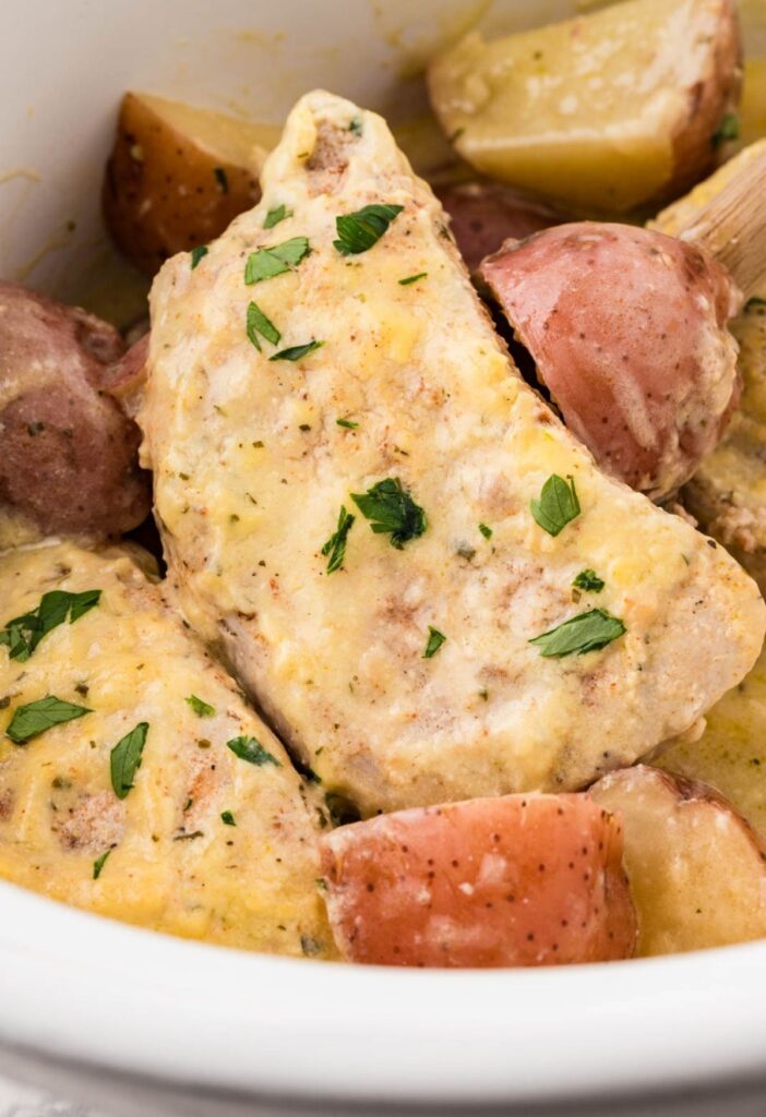 Close up of the pork chops on a wooden serving spoon inside the slow cooker.