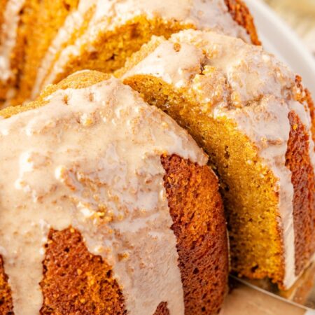 Baked pumpkin bundt cake on a white plate with a glaze, a serving spatula taking a slice from the cake.