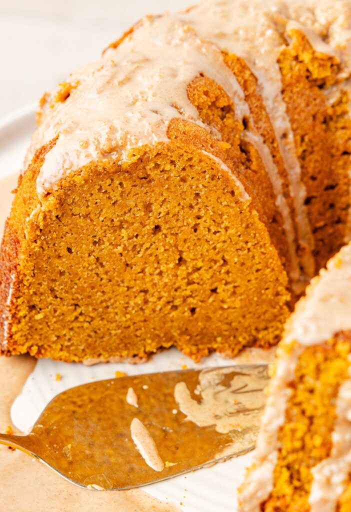 Pumpkin bundt cake on a white cake stand showing the center and how moist it is.
