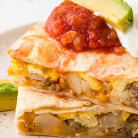 A baked quesadilla with breakfast ingredients inside topped with sour cream and salsa.
