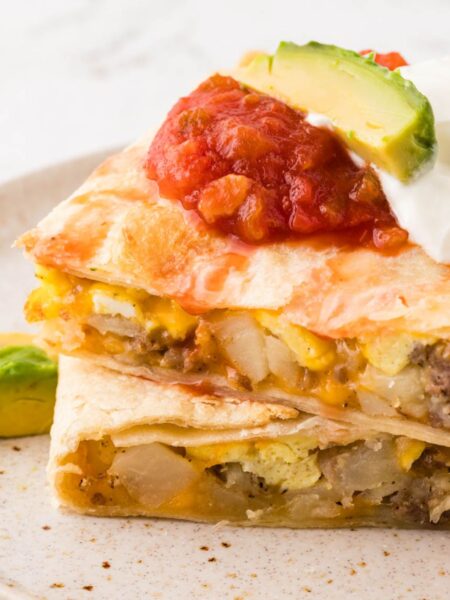 A baked quesadilla with breakfast ingredients inside topped with sour cream and salsa.
