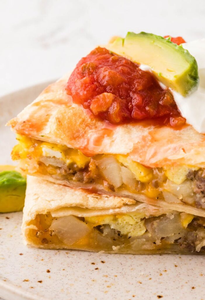 A baked quesadilla with breakfast ingredients inside topped with sour cream and salsa.