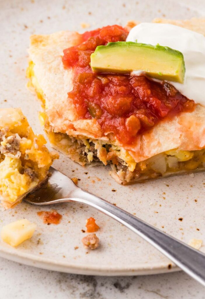 A breakfast quesadilla on a white plate with a fork.