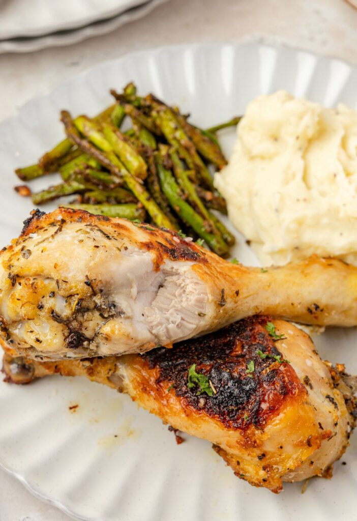 A chicken drumstick on a white plate with it torn open to see the tender chicken inside.