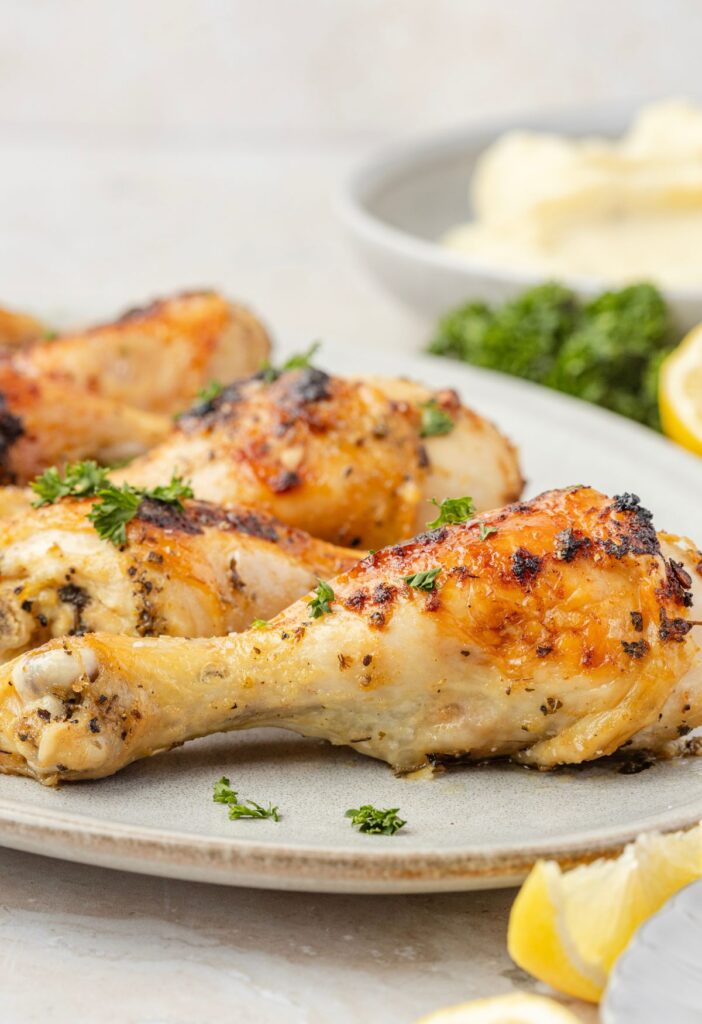 Side view of the baked chicken drumsticks on a plate with lemon and parsley.