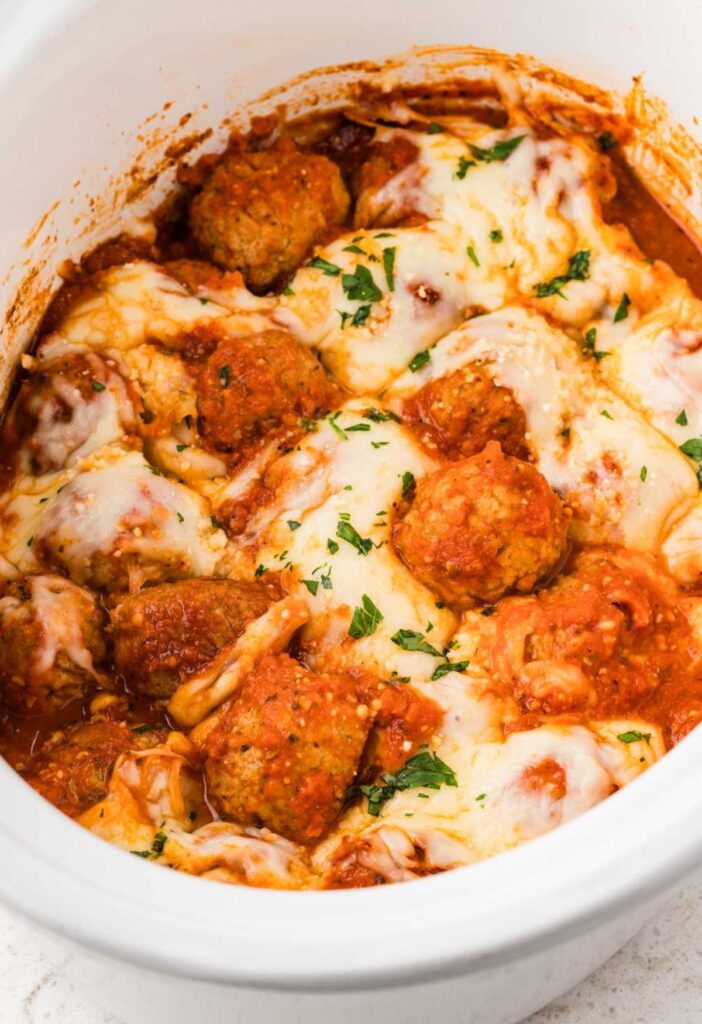 A white crockpot with the baked chicken parm meatballs inside of it.