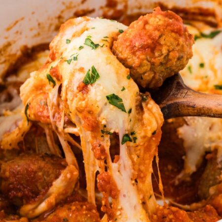 A serving spoon with a cheese pull underneath it of the parmesan chicken meatballs.