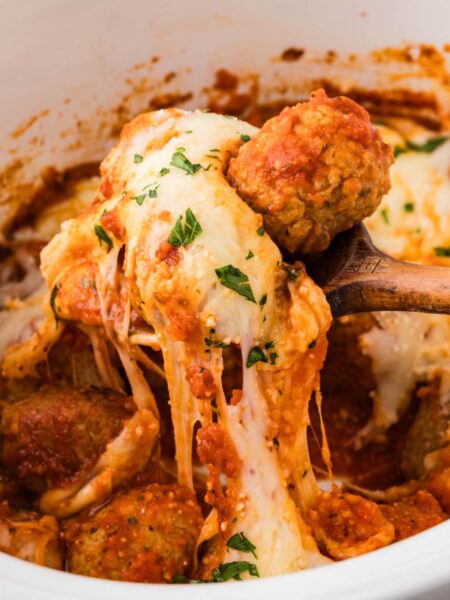 A serving spoon with a cheese pull underneath it of the parmesan chicken meatballs.