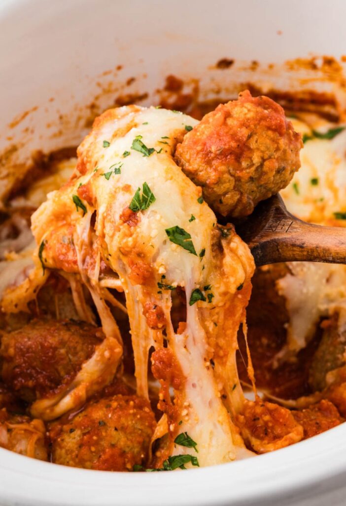 A serving spoon with a cheese pull underneath it of the parmesan chicken meatballs.