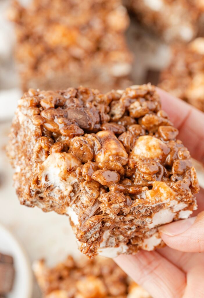 A hand holding a krispie treat with a bite taken out of it