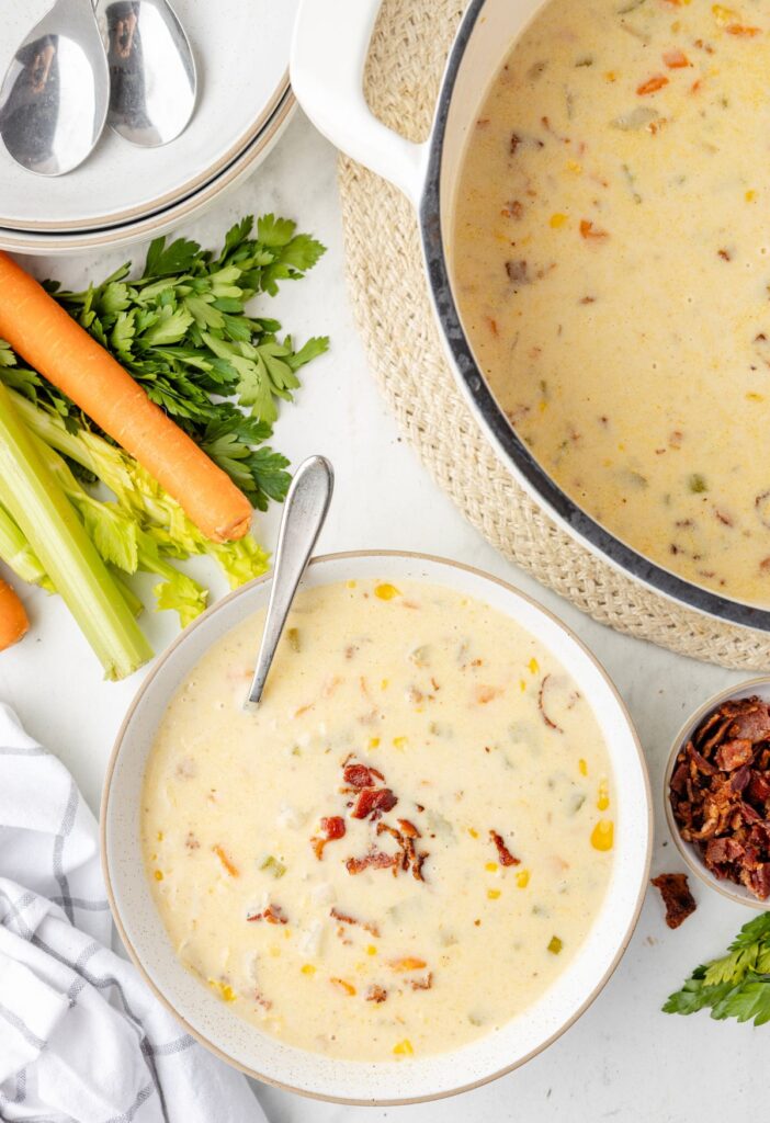 Top view of the bowl of corn and potato chowder with a serving bowl of it next to the soup pot.