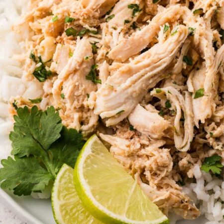 Shredded cilantro lime chicken on a white plate with cilantro and a lime wedge.