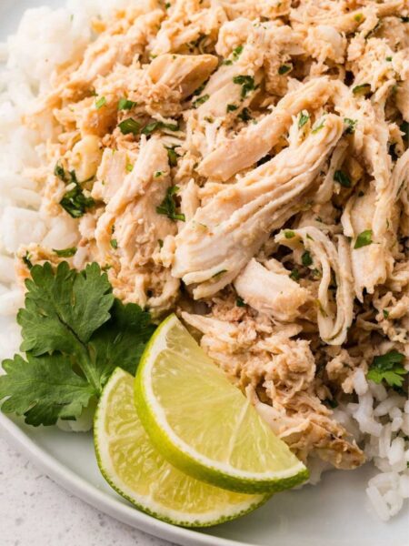 Shredded cilantro lime chicken on a white plate with cilantro and a lime wedge.