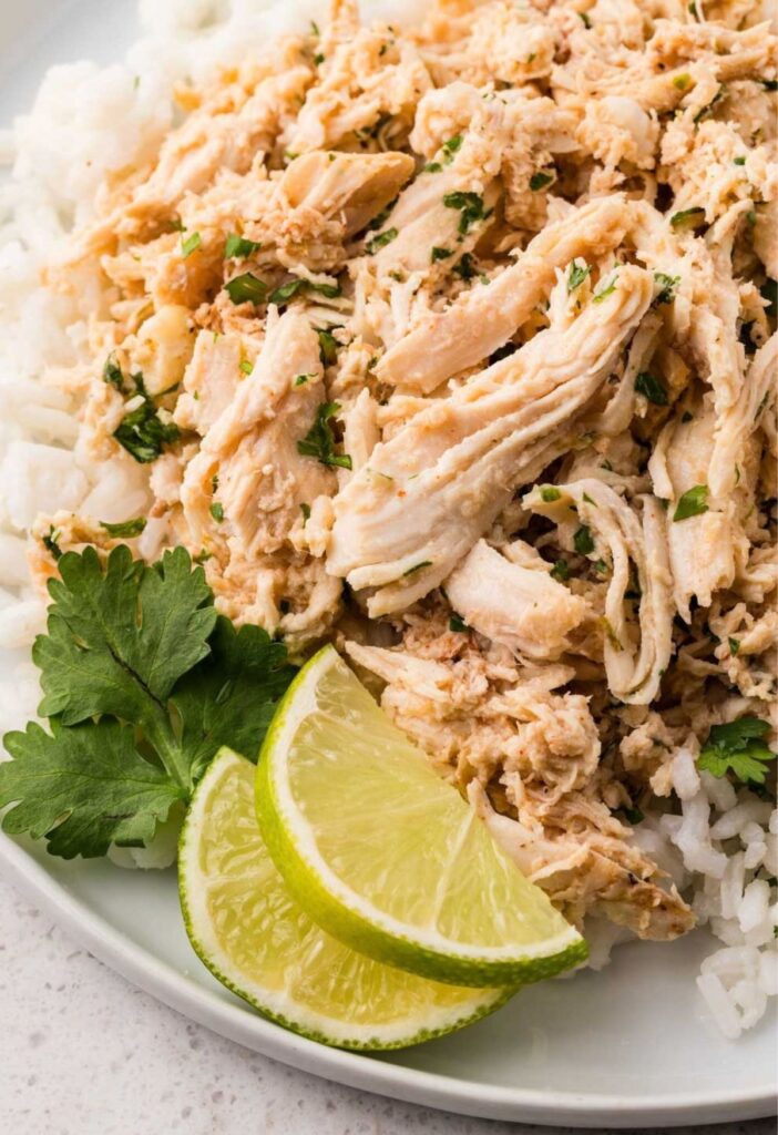 Shredded cilantro lime chicken on a white plate with cilantro and a lime wedge.