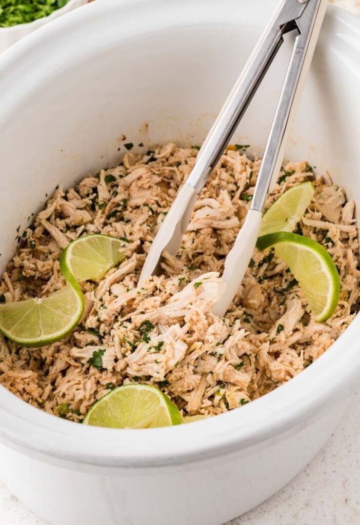 Tongs inside the crockpot with the shredded chicken.
