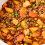 Ground beef stew made in the crockpot inside a white slow cooker.