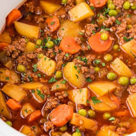 Ground beef stew made in the crockpot inside a white slow cooker.