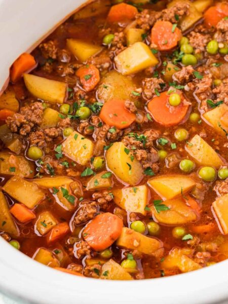 Ground beef stew made in the crockpot inside a white slow cooker.
