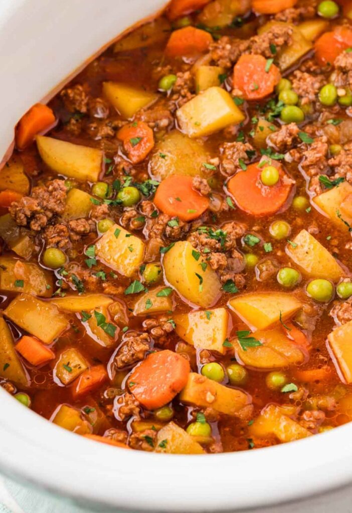 Ground beef stew made in the crockpot inside a white slow cooker.