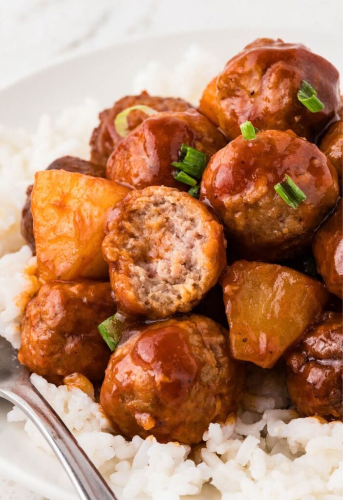 Meatballs over rice with a meatball having a bite taken out of it.