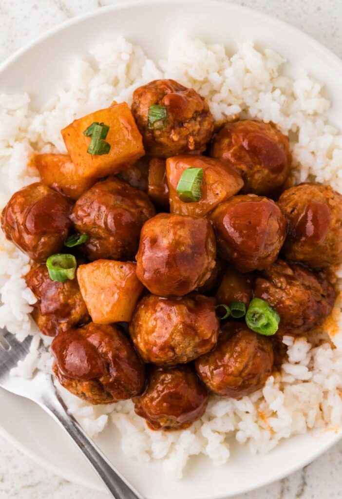 Pineapple bbq meatballs served over rice on a white plate.