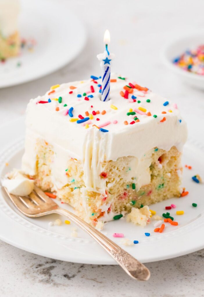 A slice of poke cake with a candle in it and a fork.