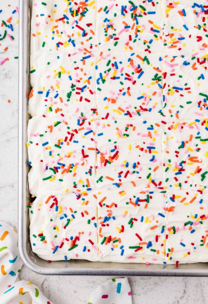 Top view of the whipped cream frosted poke cake with colorful sprinkles.