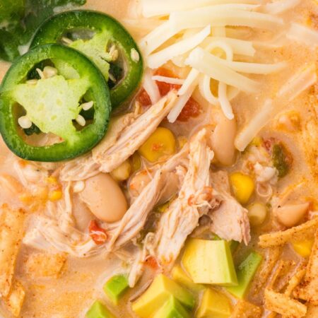 Bowl of white chicken chili with toppings like jalapeno, cheese, and tortilla strips.