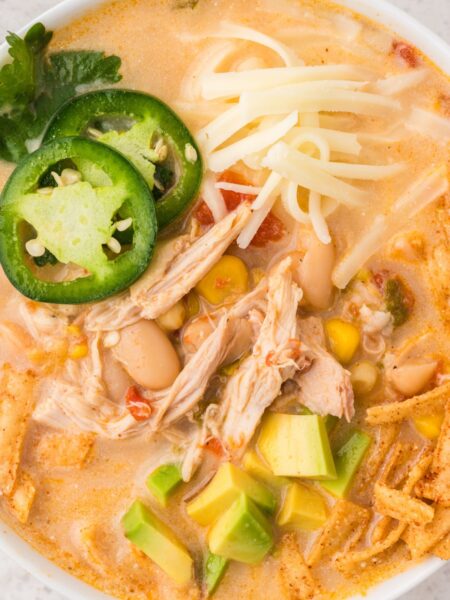 Bowl of white chicken chili with toppings like jalapeno, cheese, and tortilla strips.