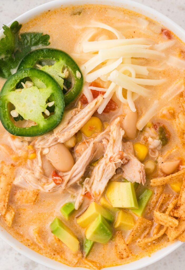 Bowl of white chicken chili with toppings like jalapeno, cheese, and tortilla strips.